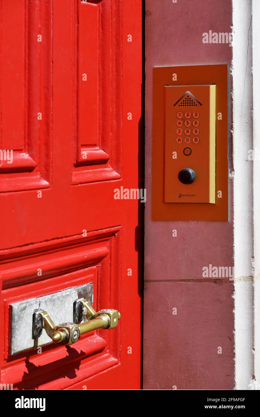 un tastierino di ingresso codice digitale e un sistema di interfono montati su una parete rosata accanto a una porta a pannelli rosso acceso a Parigi, Francia Foto Stock