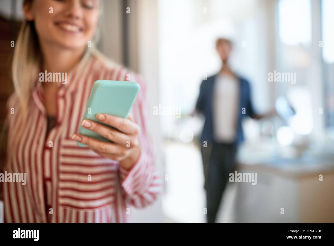 bella giovane bionda adulta che tiene il suo telefono cellulare, a fuoco, con la persona blurry nel campo di bellezza Foto Stock