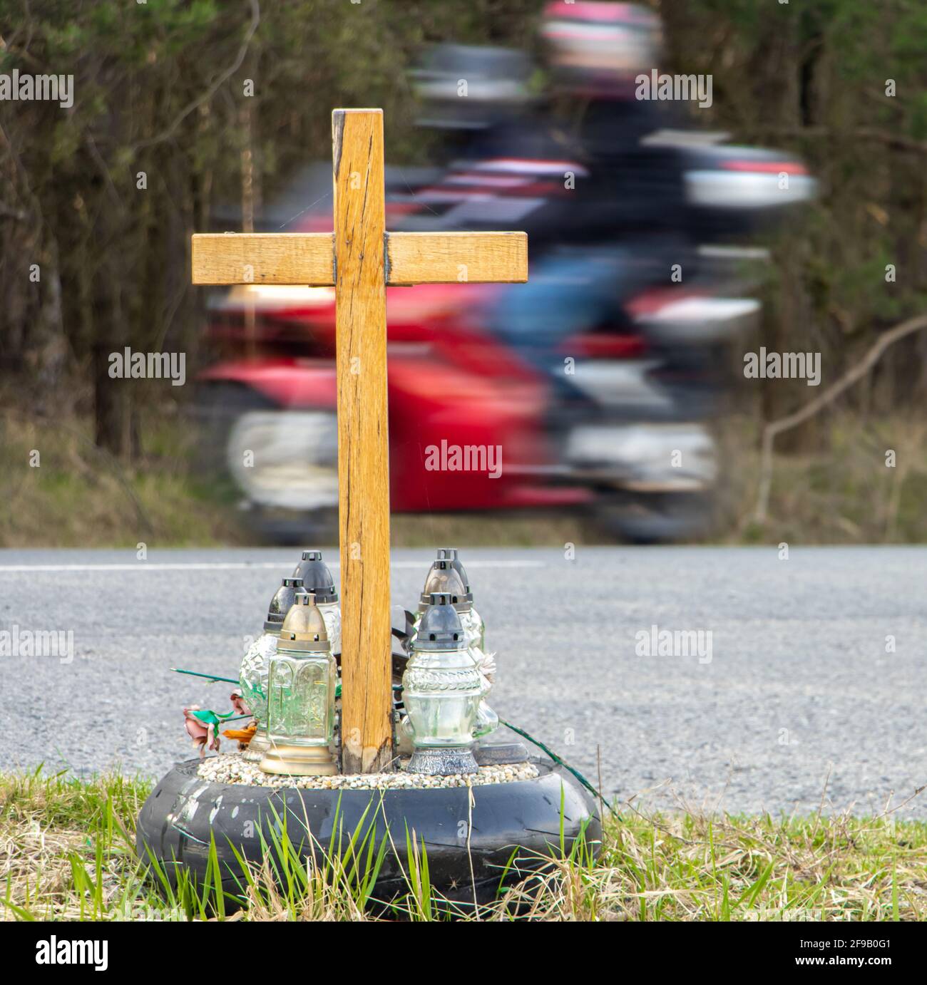 Una croce commemorativa a lato della strada con candele che commemorano la tragica morte, su un percorso di sfondo moto offuscata Foto Stock
