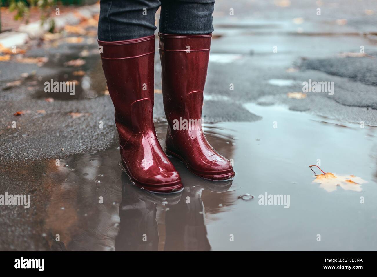 I piedi femmina in gomma rossa stivali in piedi in un fangoso puddle sotto la pioggia nel tempo di autunno Foto Stock