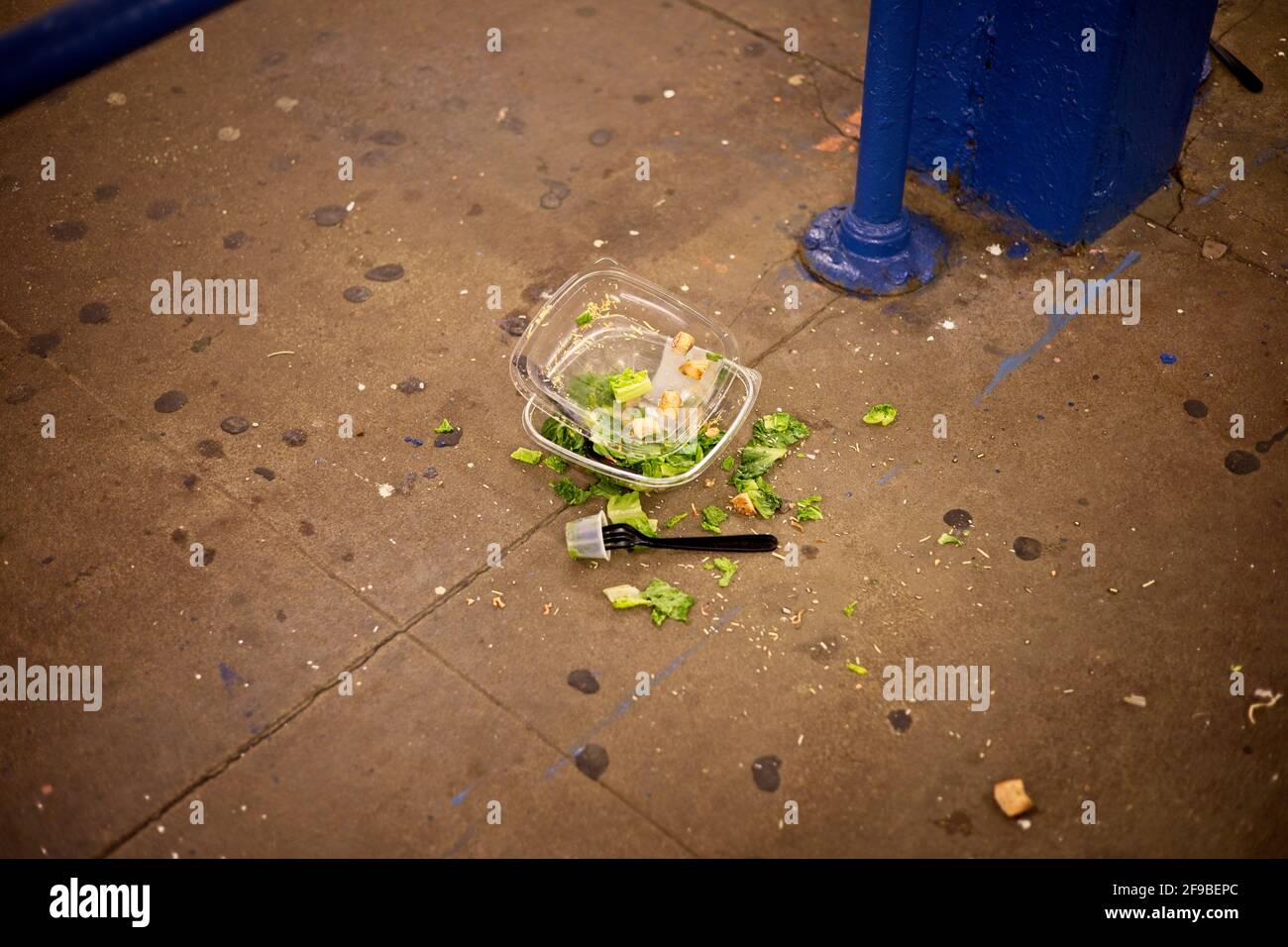 Contenitore per pranzo in plastica con insalata caduto sul marciapiede vicino un supporto metallico Foto Stock