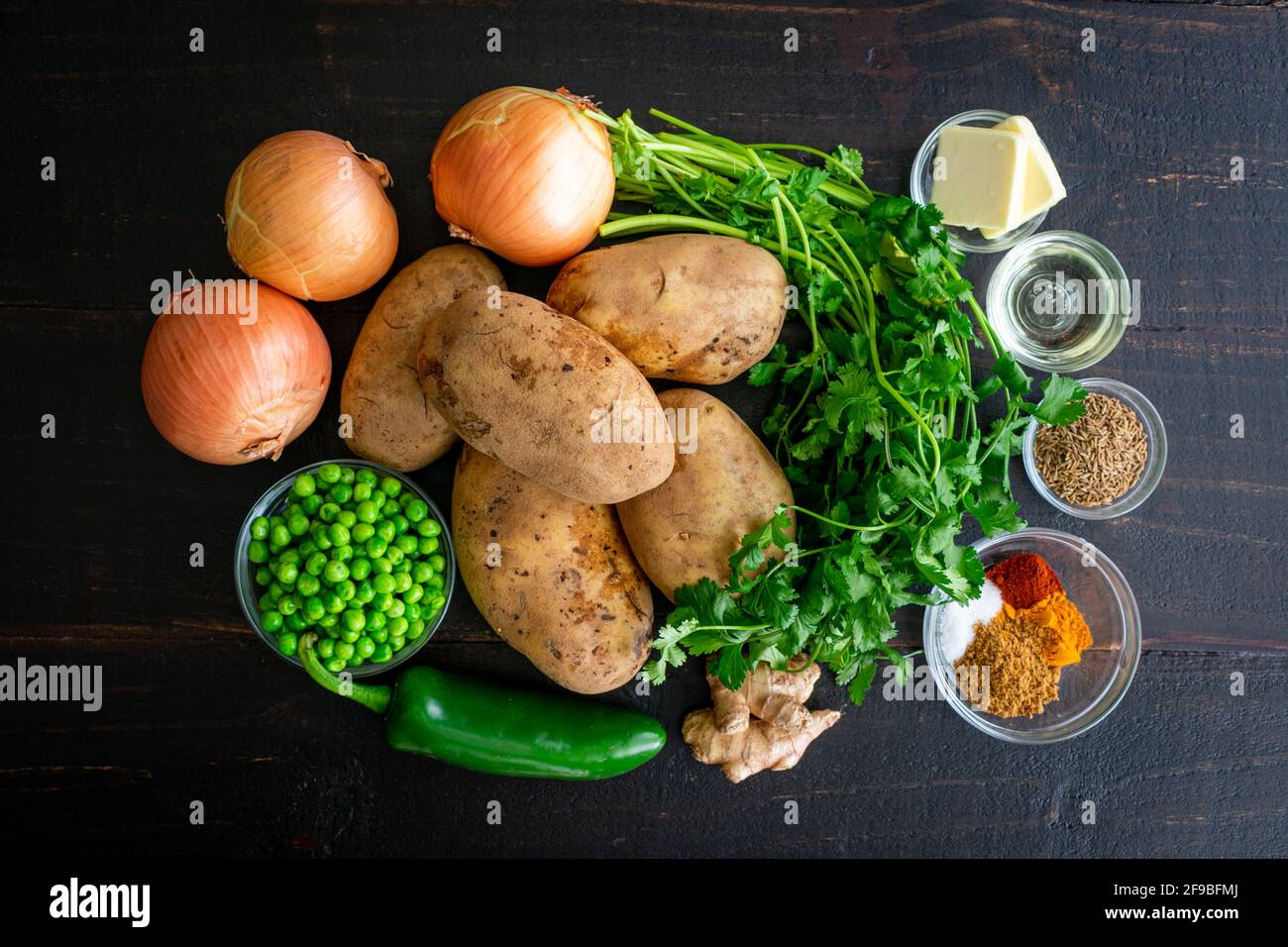 Patate di samosa ingredienti su un legno scuro sfondo: Patate crude, cipolle, piselli, erbe e spezie su un tavolo di legno Foto Stock