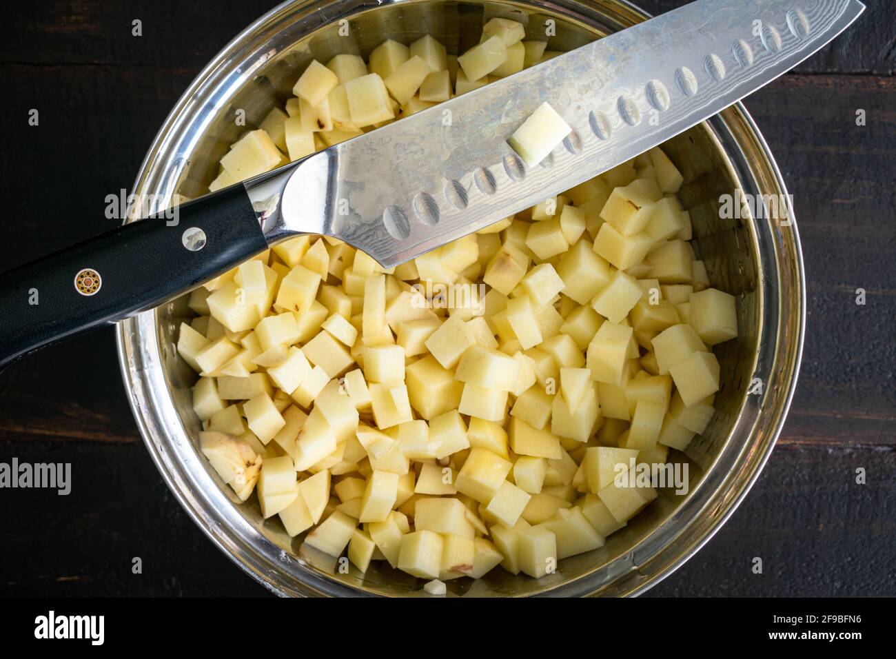 Patate russet a dadini e un coltello dello chef: Una ciotola di miscelazione piena di patate russet ortografate e tagliate a cubetti con un coltello santoku Foto Stock