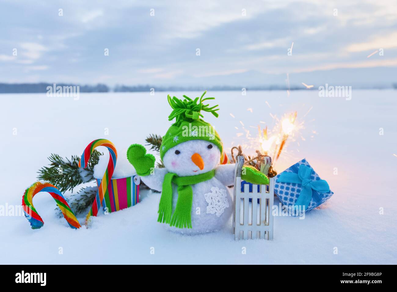 Pupazzo di neve divertente con slitta, caramelle colorate, scatola regalo e sparklers. Felice anno nuovo 2020. Composizione natalizia con fondo nevoso. Foto Stock