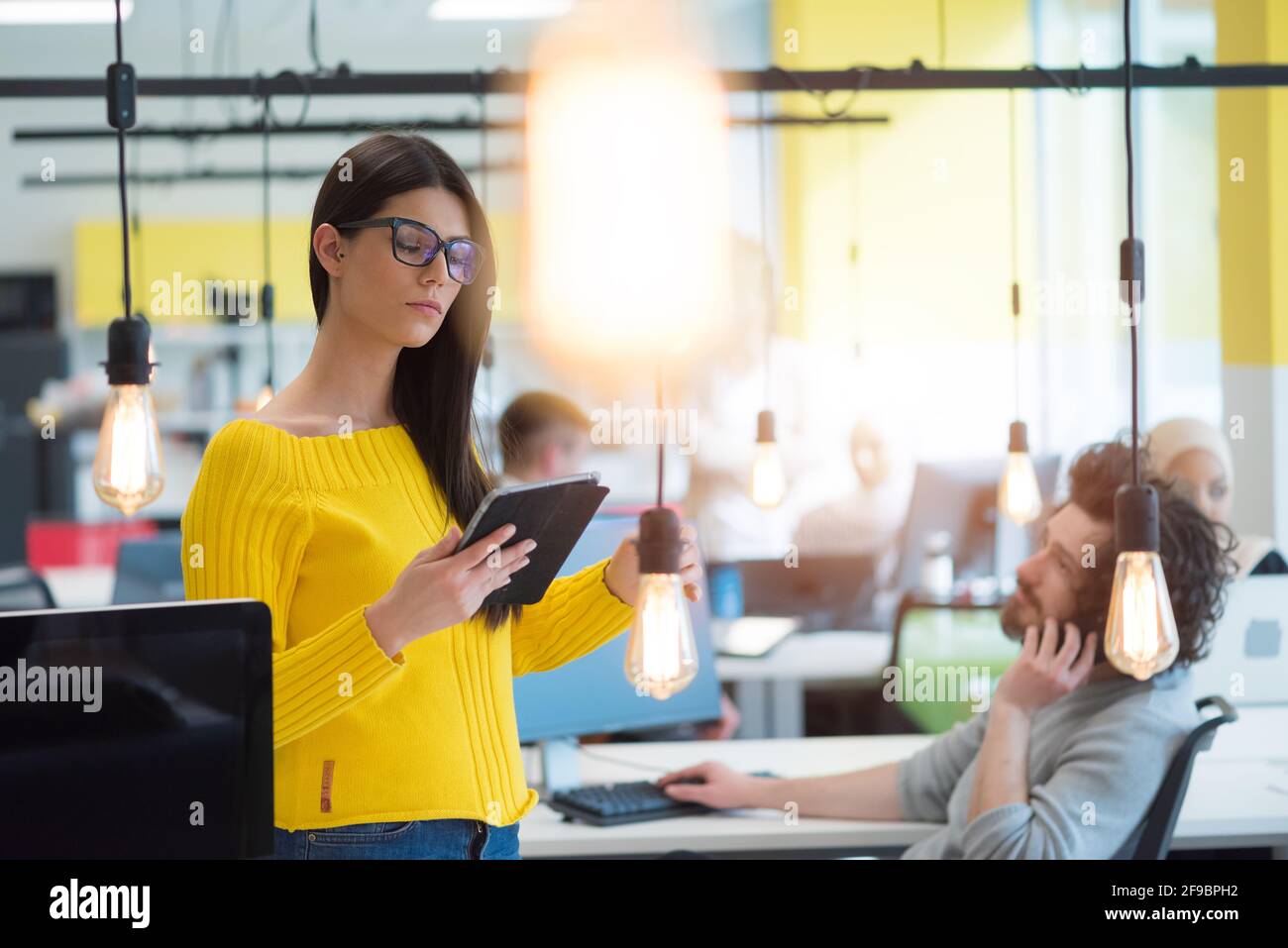 Ritratto di giovane bella ragazza casual felice businesswoman in piedi con il laptop al suo posto di lavoro all'interno di moderno co-working space. Foto Stock