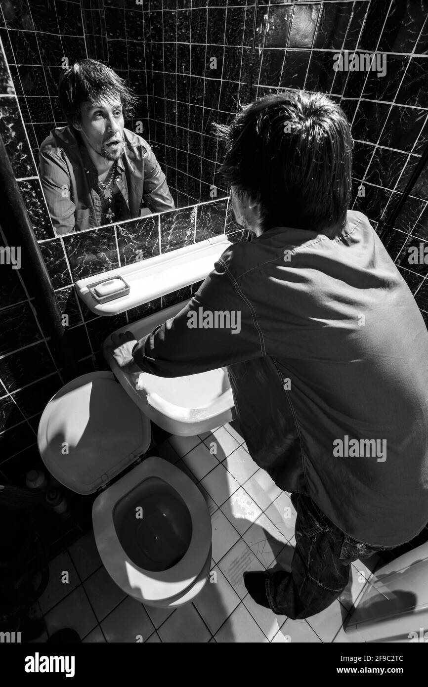 L'uomo ubriaco si guarda nello specchio in un bagno Foto Stock