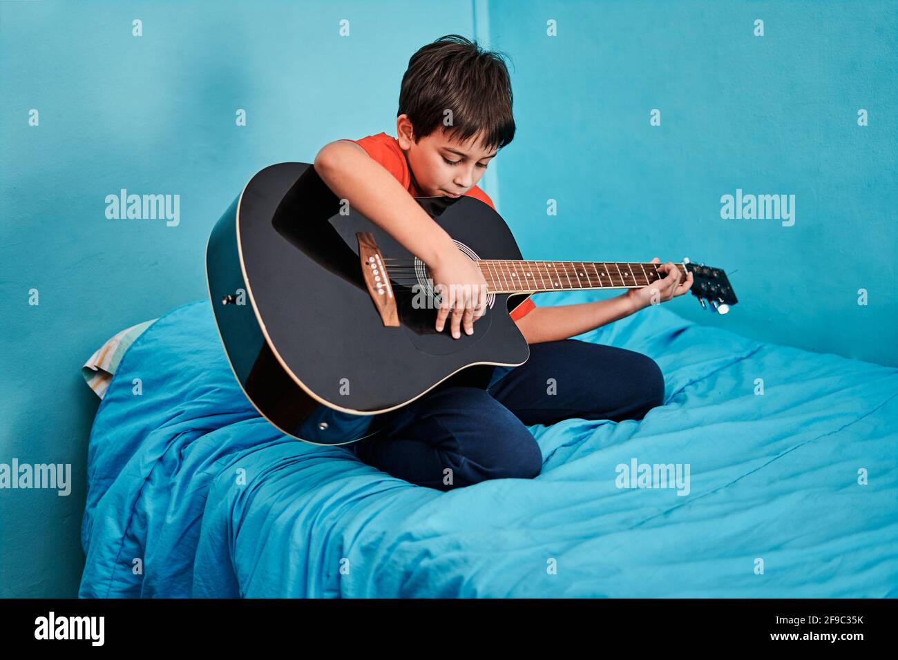 Ragazzo che suona la chitarra sul letto in camera a. casa Foto Stock
