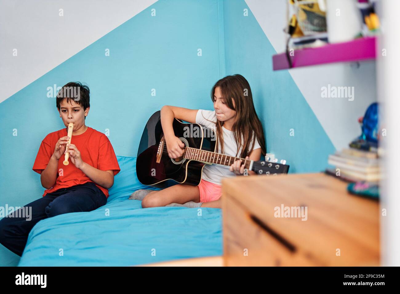 Ragazzo e ragazza che suonano chitarra e flauto in cima letto in camera Foto Stock