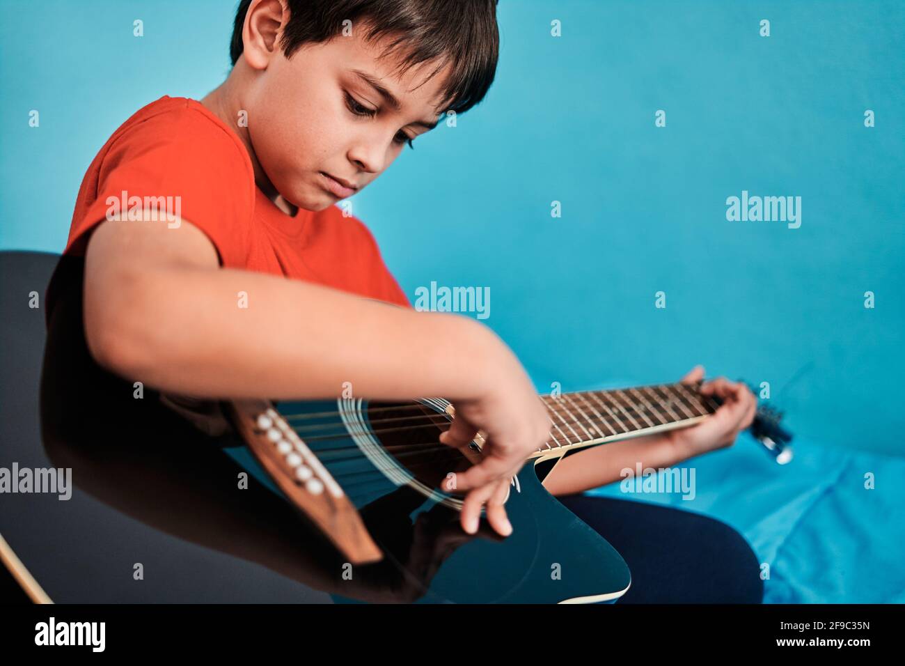 Primo piano del ragazzo che suona la chitarra sopra il letto dentro camera a casa Foto Stock
