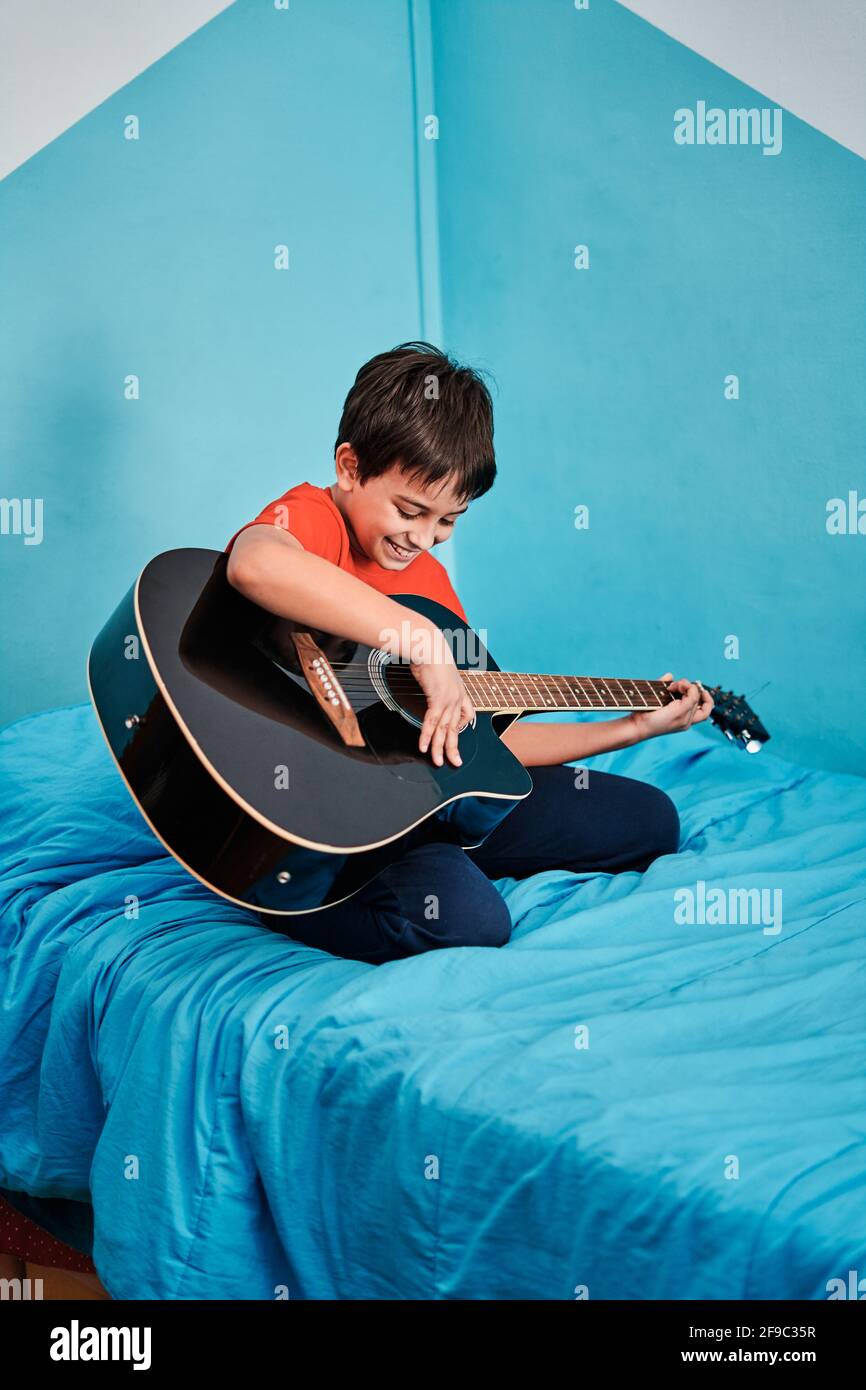 Ragazzo che suona la chitarra sul letto in camera a. casa Foto Stock