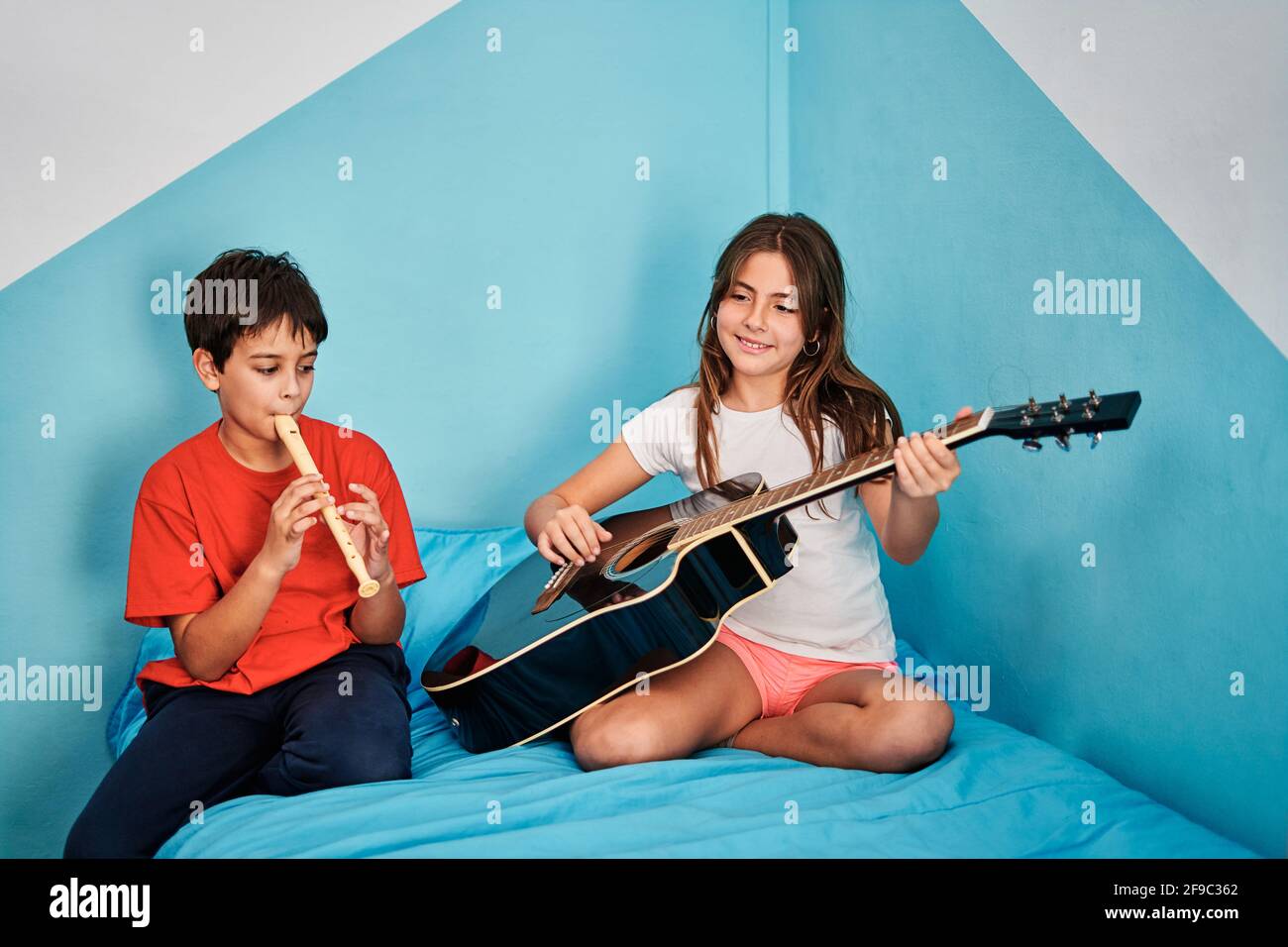 Ragazzo e ragazza che suonano chitarra e flauto in cima letto in camera Foto Stock