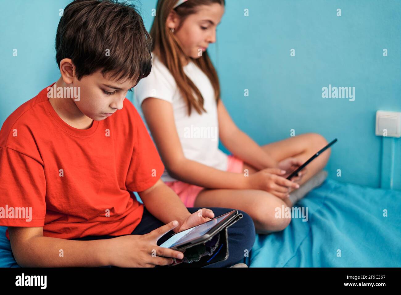 Ragazzo e ragazza seduti a letto guardando il tablet dentro camera a casa Foto Stock