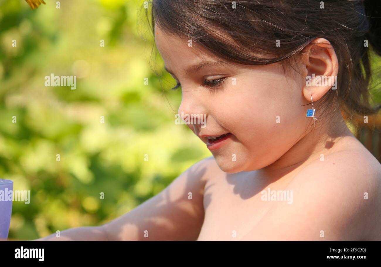 primo piano ritratto di una bambina ridente con una coda di pontile sulla natura estiva sullo sfondo di foglie verdi sfocate Foto Stock