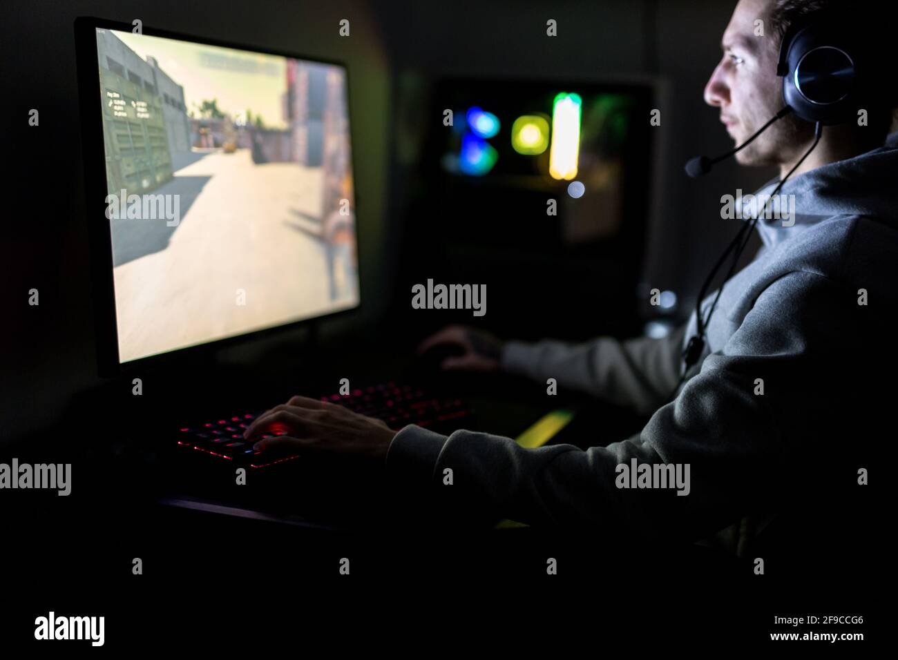 Videogamer professionista o Streamer giocare a Sparatutto in prima persona Video Game online su un PC di gioco personalizzato. Indossa una cuffia Foto Stock