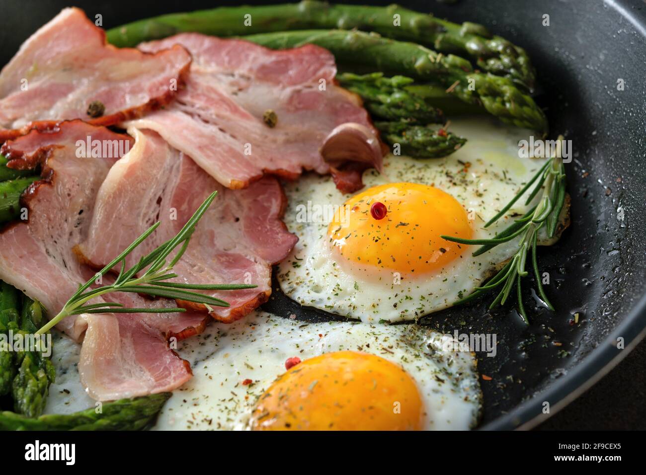 Asparagi fritti con pancetta, uova e spezie su una padella in primo piano Foto Stock