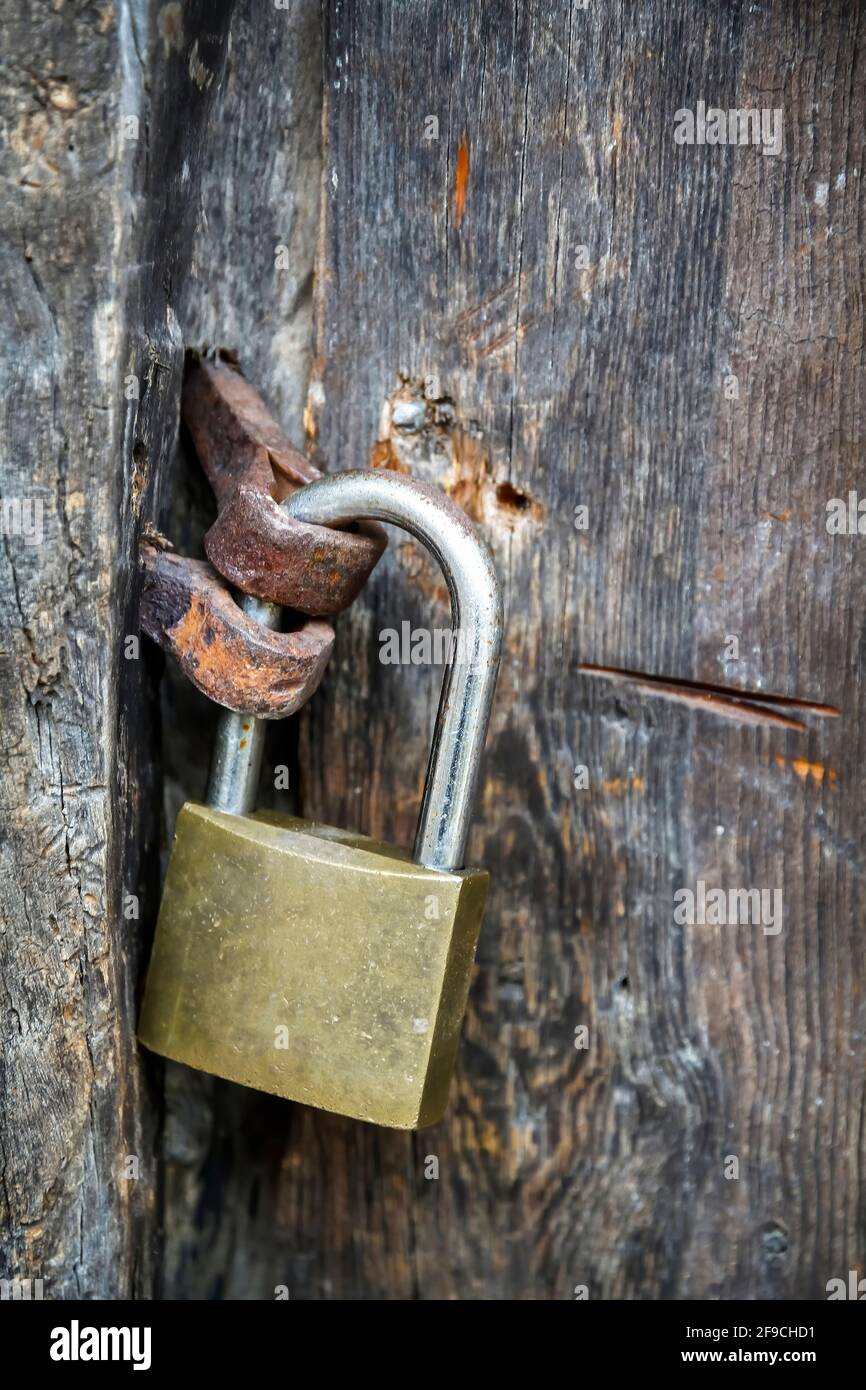 Una porta in legno invecchiato e strutturato con un lucchetto, chiavistello  e accessori in metallo.