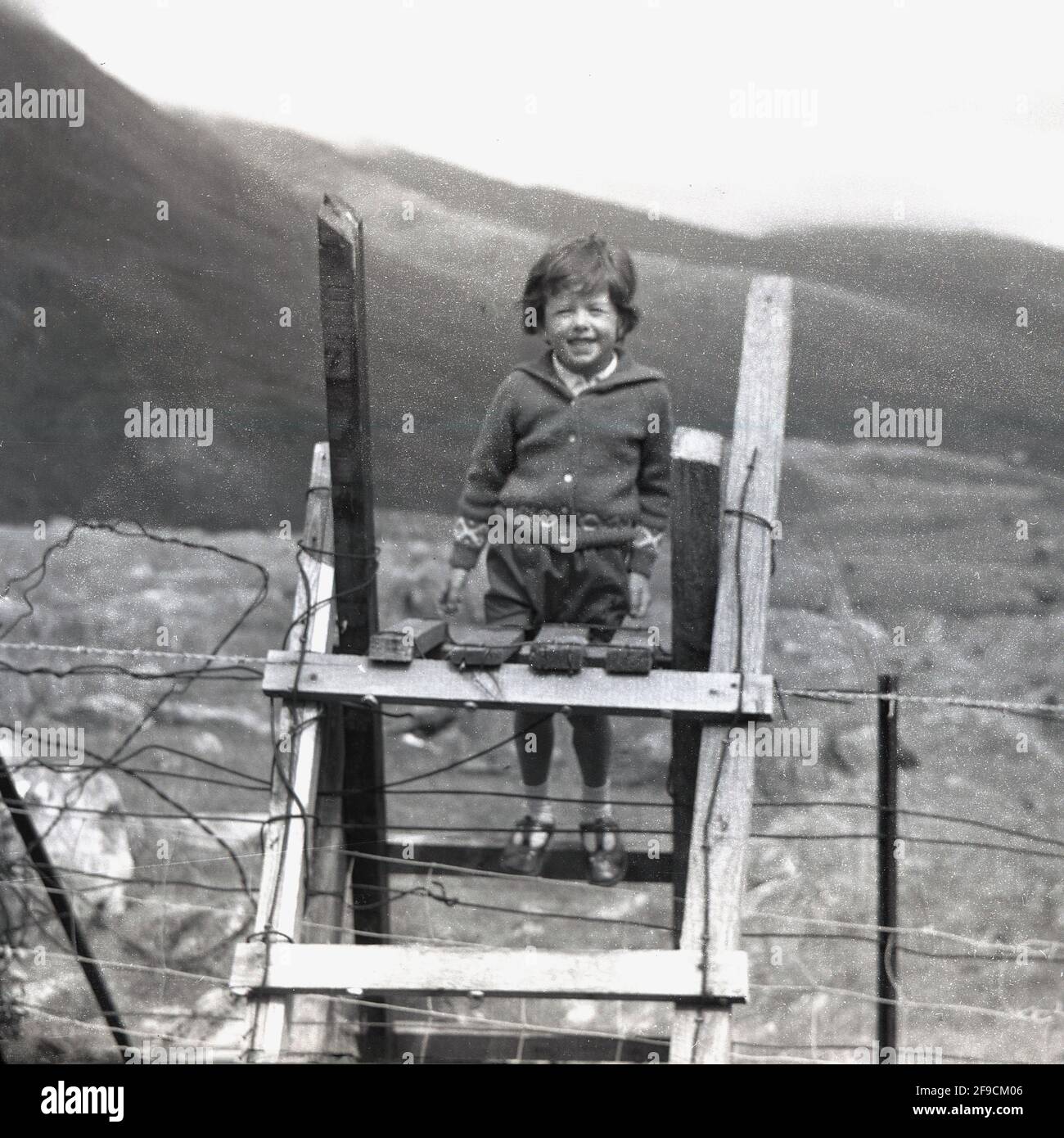 Anni '60, storica, al di fuori delle valli dello Yorkshire, una giovane ragazza in piedi sui gradini di una stiglia di legno su un recinto di filo spinato. Uno stile è una serie di passi che permette di superare una recinzione o una barriera, vale a dire, il trasferimento da un campo al successivo, ma impedisce qualsiasi animale da fattoria o bestiame fuga, Inghilterra, Regno Unito. Foto Stock