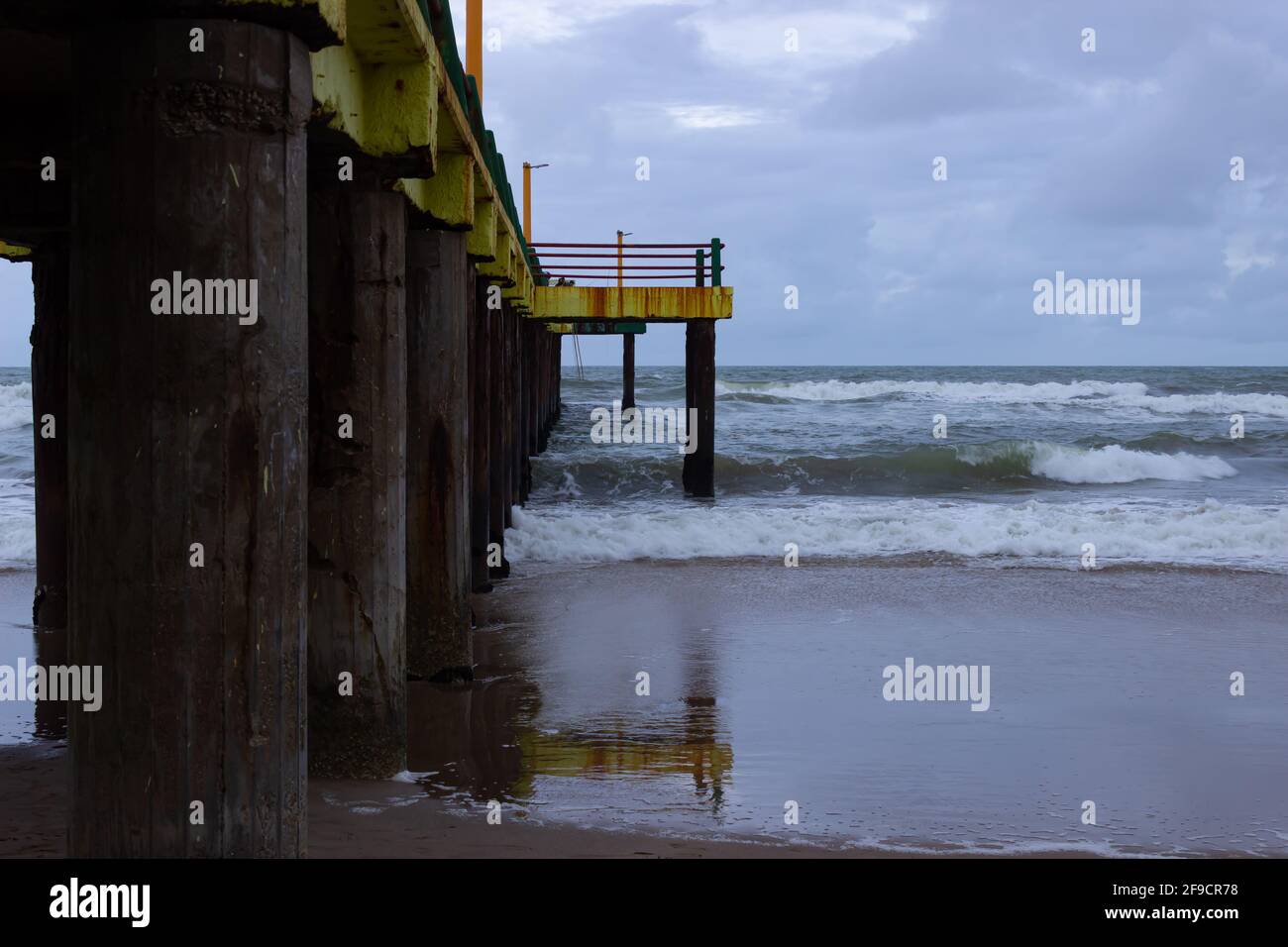 Onde che colpiscono un vecchio molo in una giornata nuvolosa. Foto Stock