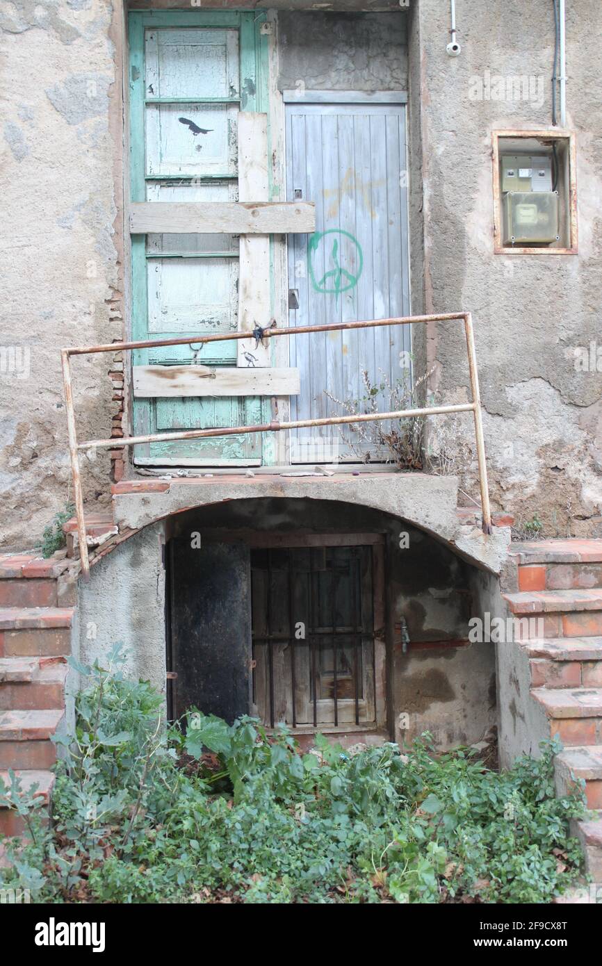 Porta chiusa abbandonata, con scala, balcone, corrimano, scatola fusibili e un cartello di pace su una porta di legno Foto Stock