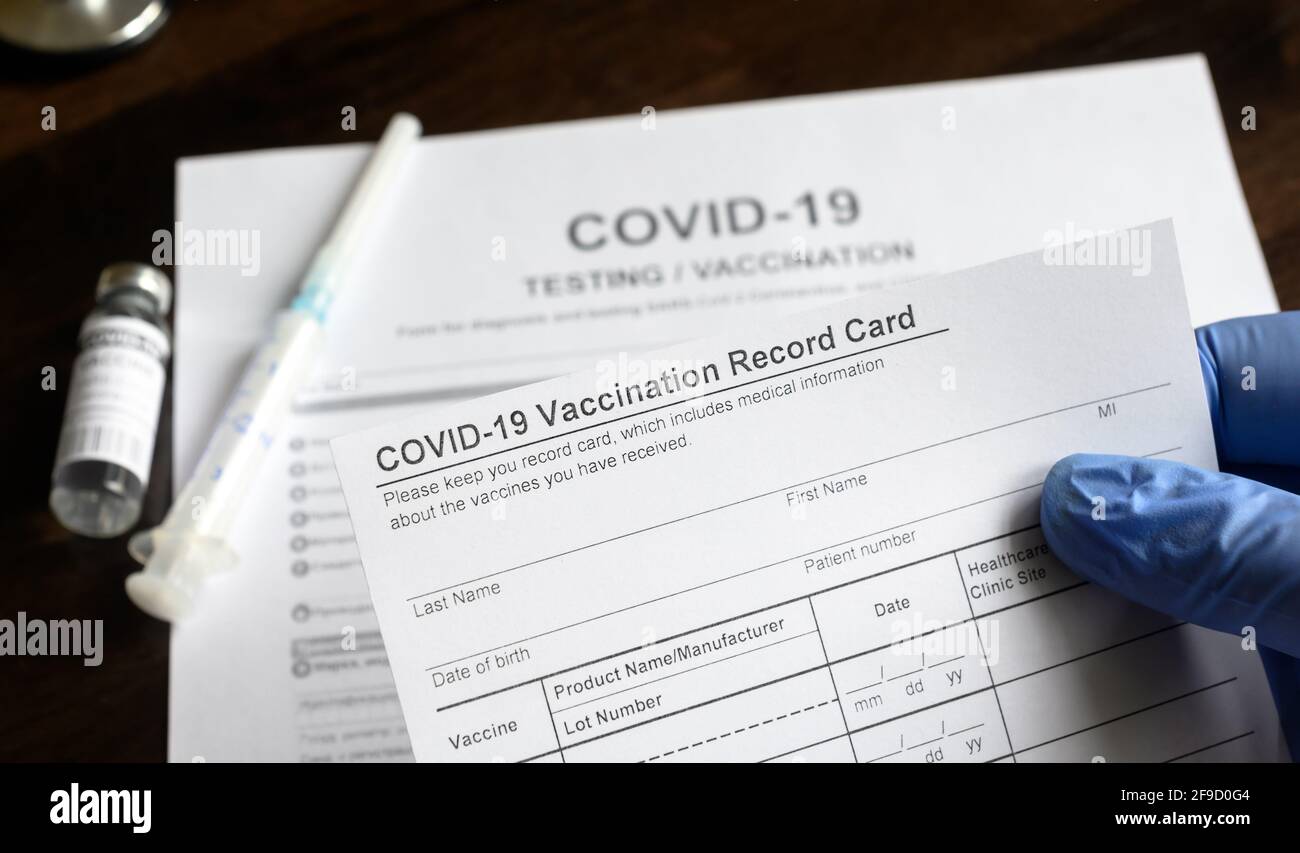 COVID-19 Vaccination Record Card in doctor hand, test del coronavirus e forma medica del vaccino alla scrivania in clinica. Concetto di cert di vaccinazione del virus corona Foto Stock