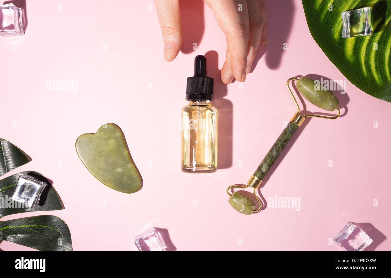 Raschietto Jade gua sha, massaggiatore a rullo e olio cosmetico. Il concetto di self-care. Parte della mano di una donna. Zero sprechi. Sistemi di sollevamento e tonificazione Foto Stock