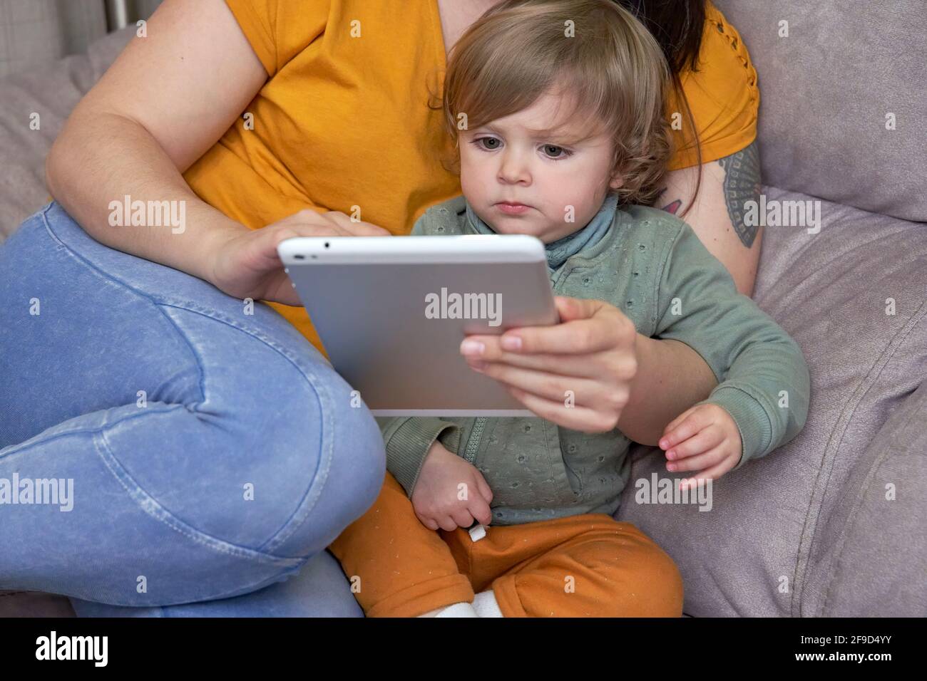 Un primo piano di una ragazza tra le braccia della madre mentre si usa un tablet. Concetto di comfort e di svago a casa. Foto Stock