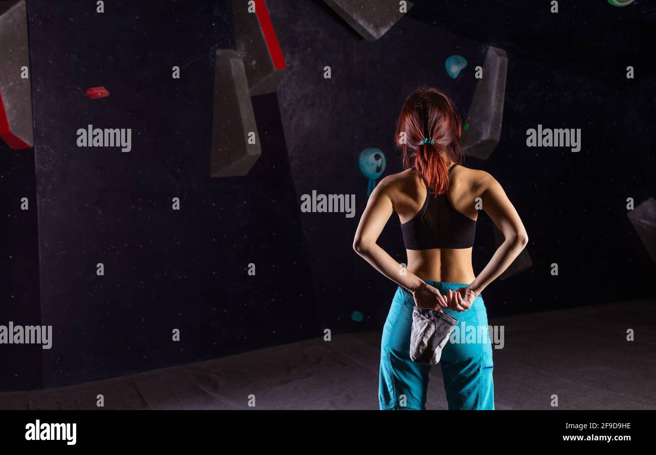 Giovane donna che si prepara a salire in bouldering palestra, calking mani e l'esame percorso sulla parete, vista posteriore Foto Stock