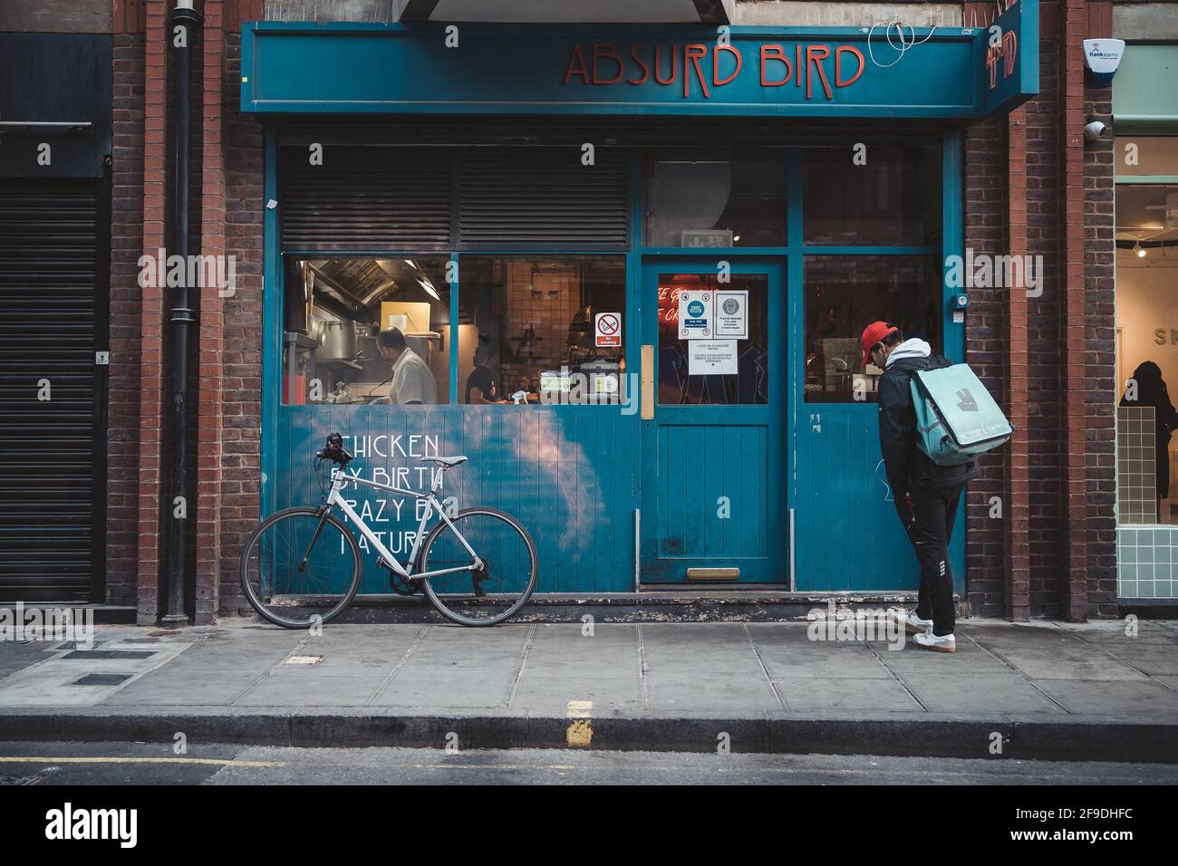 Soho, Londra | UK - 2021.04.16: Pilota uomo Deliveroo con una moto in attesa di nuovo ordine. Servizio di consegna Foto Stock