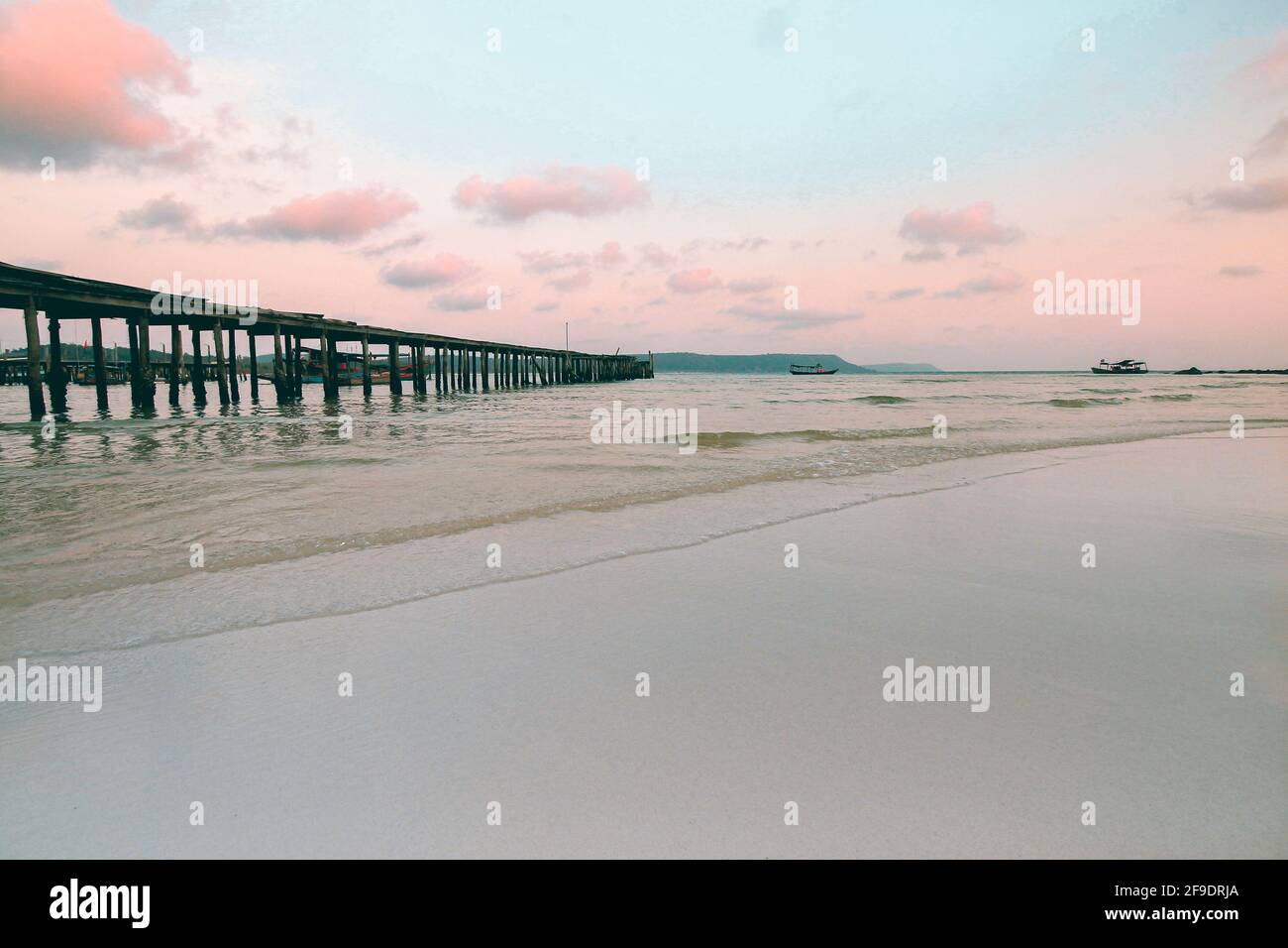 Un vecchio molo di legno su una spiaggia di sabbia bianca a. tramonto Foto Stock