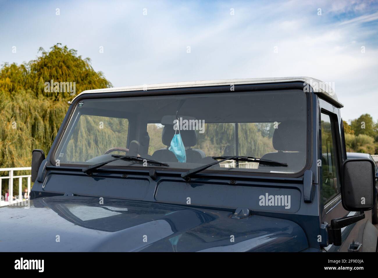 Una maschera facciale è appesa allo specchietto retrovisore di una Land Rover Defender marina. Cambridge, Regno Unito. Foto Stock