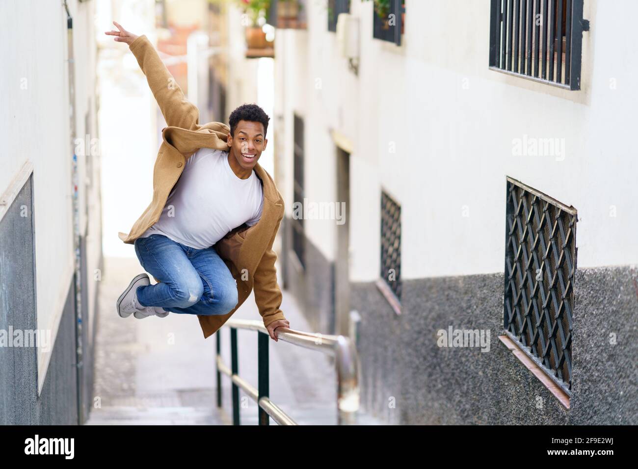 Giovane uomo nero che salta per gioia su un corrimano in strada. Foto Stock
