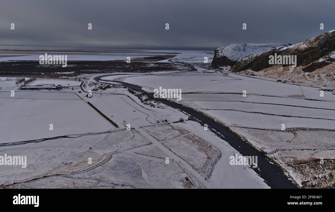 Splendida vista aerea della costa meridionale dell'Islanda con il tortuoso fiume Skógá vicino a Skógafoss e l'oceano Atlantico all'orizzonte durante la giornata invernale nuvolosa. Foto Stock