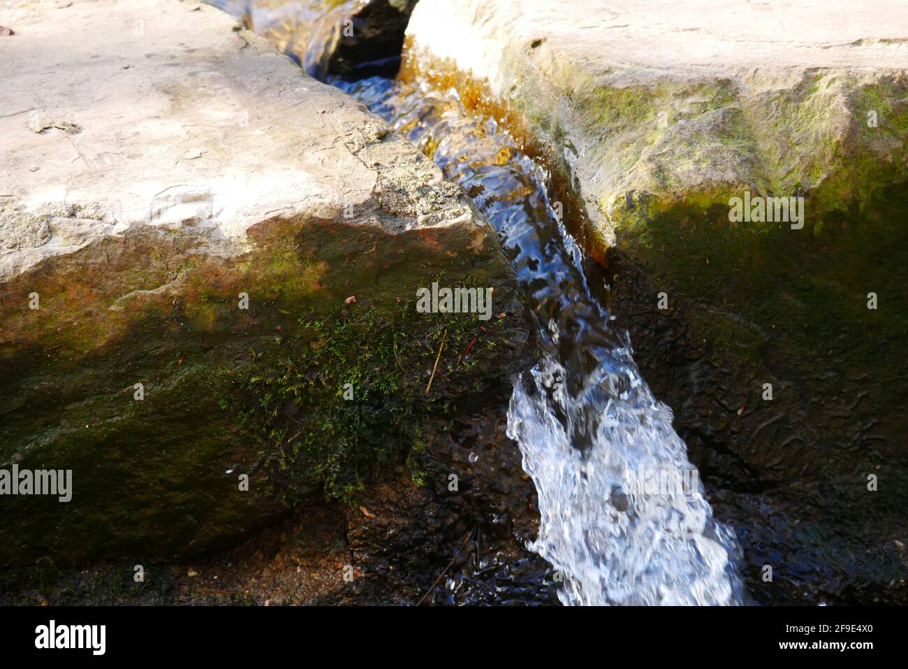 piccola cascata tra grandi blocchi di pietra nella luce del sole vicino una fonte Foto Stock