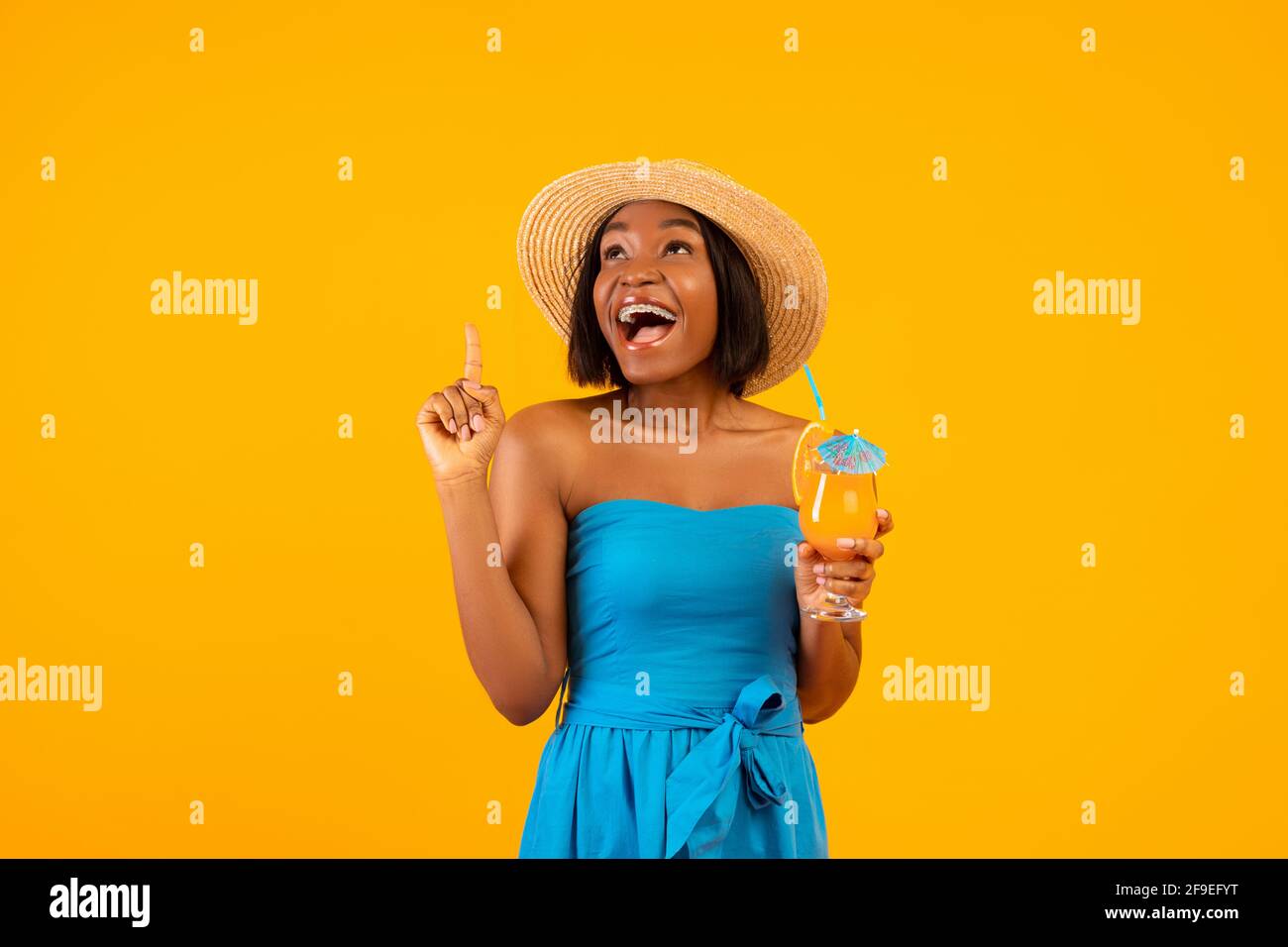 Millennial black lady con yummy cocktail tropicale urlando WOW e. rivolto verso l'alto sullo sfondo arancione dello studio Foto Stock