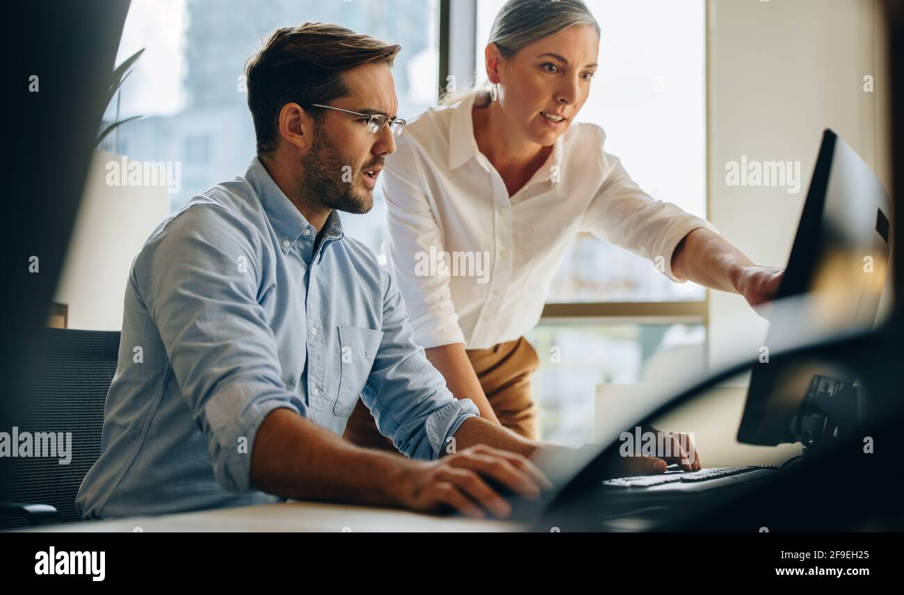 Manager punta sullo schermo del computer e parla del lavoro con un collega. Collega che aiuta l'uomo a migliorare la relazione. Foto Stock
