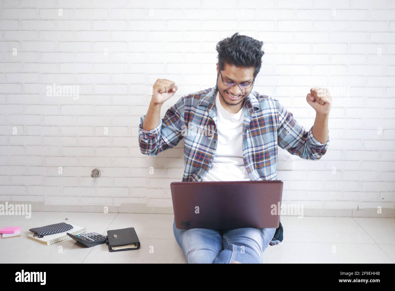 Concetto di lavoro da casa, felice giovane uomo seduto a terra che lavora su un computer portatile Foto Stock