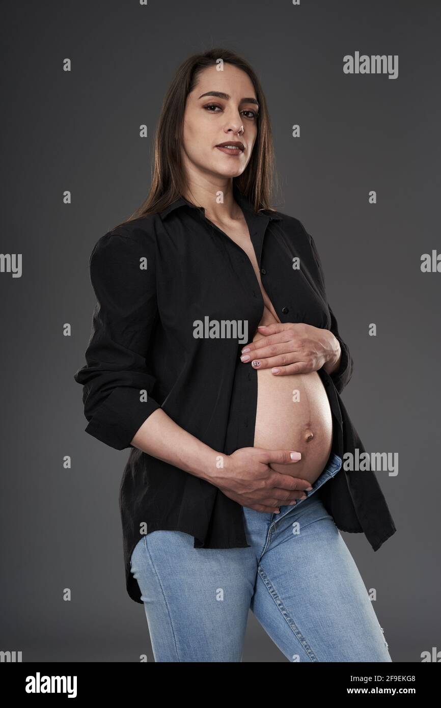 Donna incinta in jeans blu e camicia nera senza bottoni in posa su sfondo  grigio Foto stock - Alamy