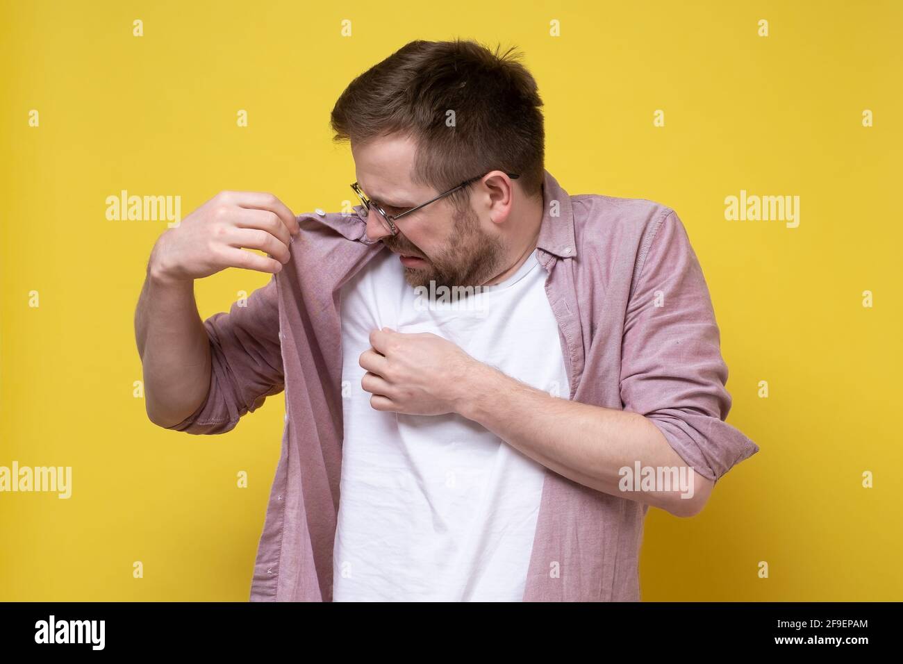 L'uomo disgridato con gli occhiali e i vestiti casual sniffa le sue ascelle, irritato dal problema del sudore e della puzza del corpo. Foto Stock