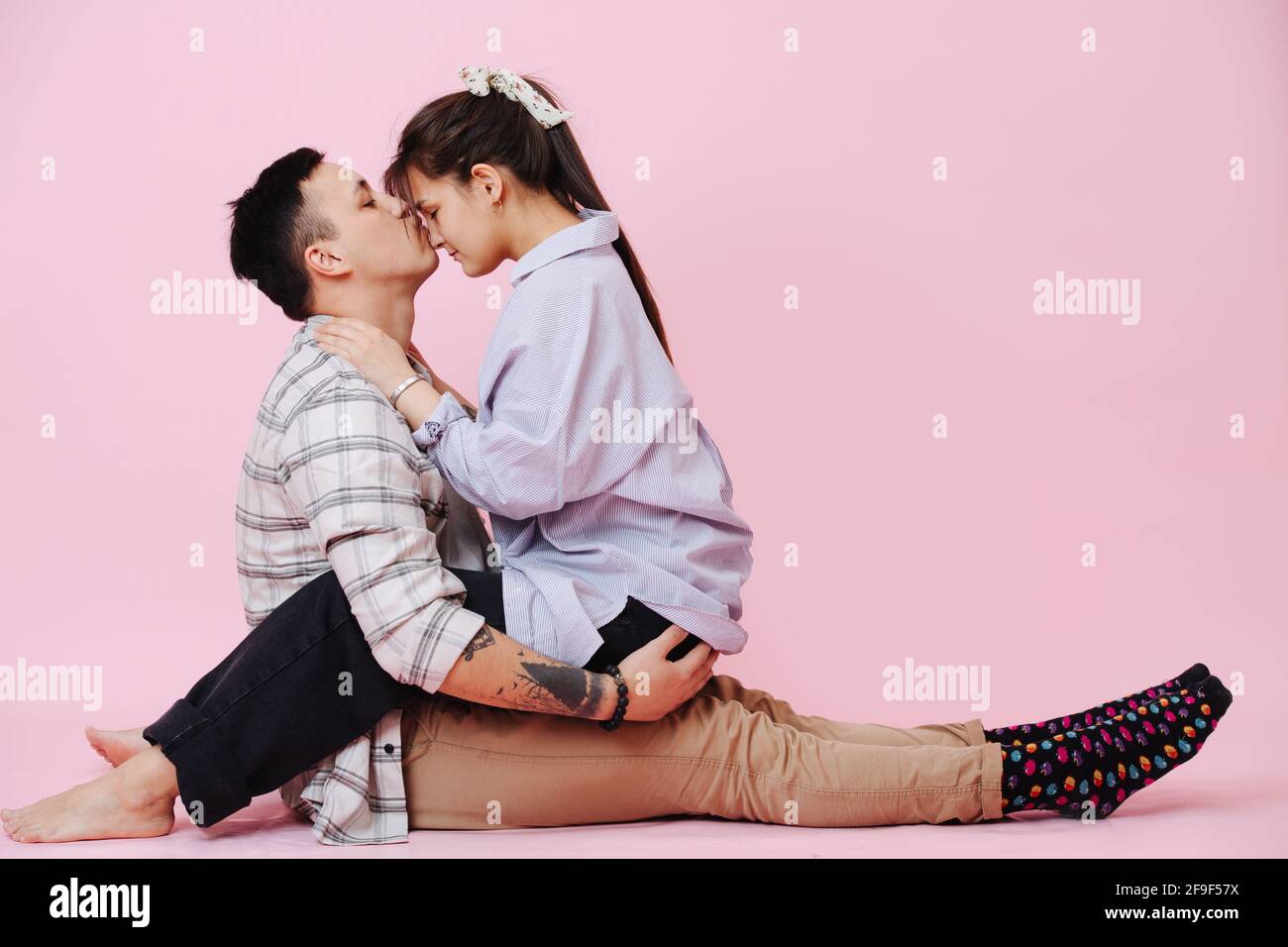 Giovane coppia in amore seduta sul pavimento, toccando le teste, ragazzo che baciano la ragazza Foto Stock