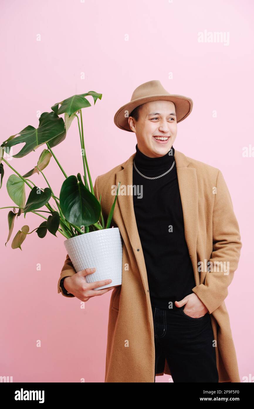Uomo di mezza età sicuro in corto cappotto beige, pentola di tenuta con pianta monstera Foto Stock