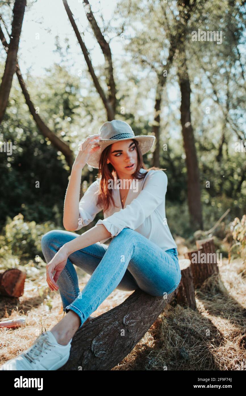 Un'immagine verticale di un'elegante donna caucasica seduta sopra un ceppo di albero in una foresta Foto Stock