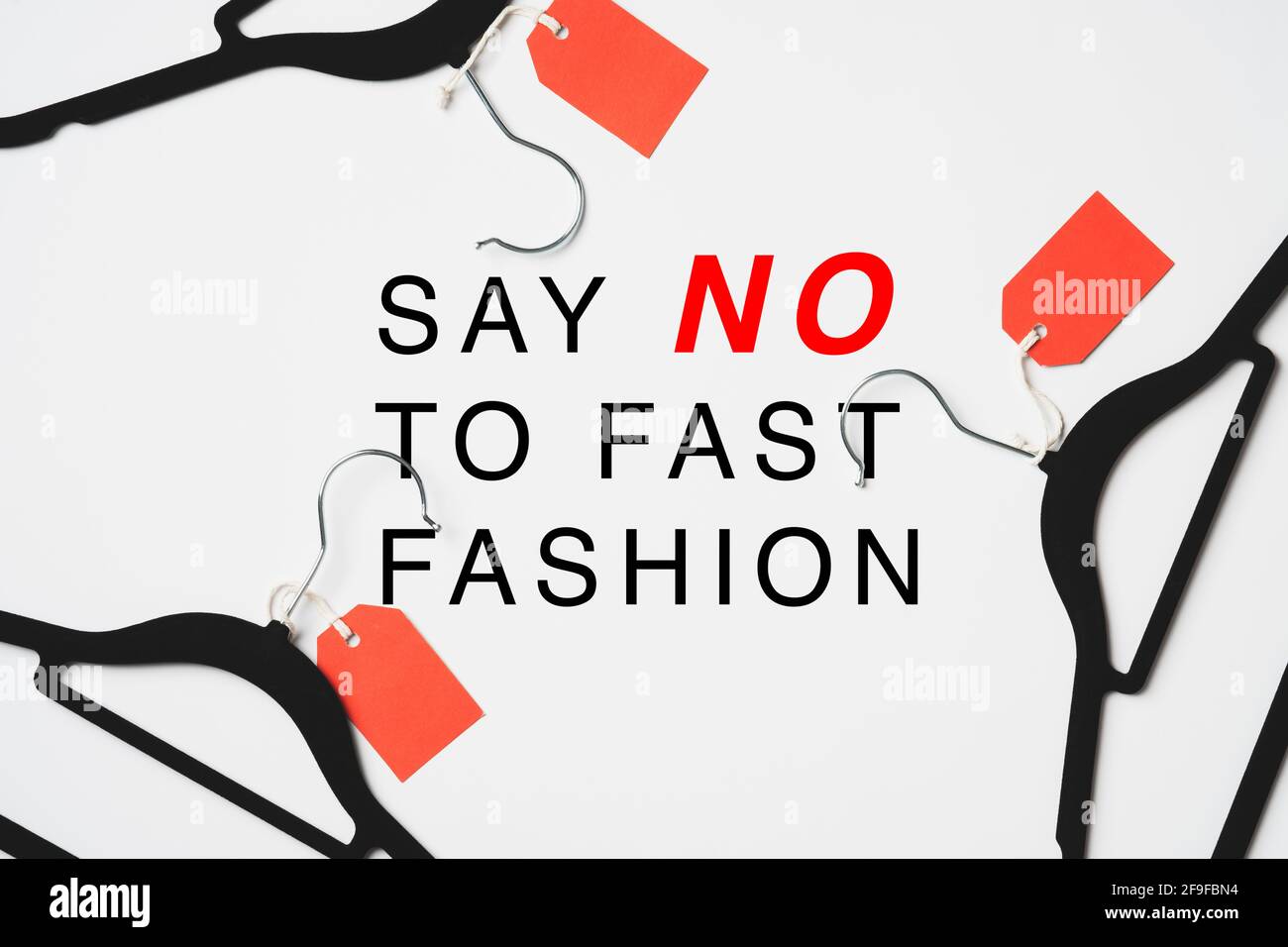 Rallenta il concetto di moda veloce. Appendiabiti neri con etichette rosse e segno 'Say NO to fast fashion' su sfondo bianco. Foto Stock