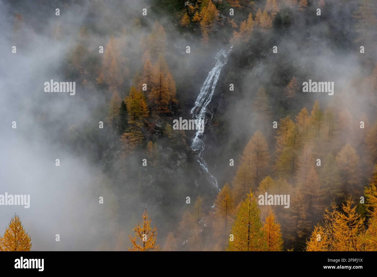Dalla nebbia della Valle emerge una piccola cascata D'Aosta Foto Stock