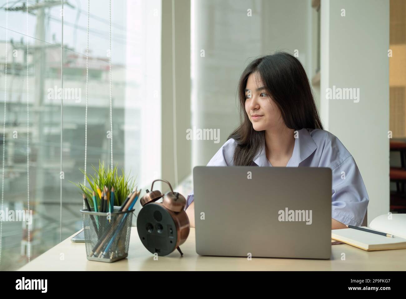 Ritratto giovane ragazza asiatica guardando la finestra all'esterno mentre usando computer portatile per l'apprendimento online Foto Stock