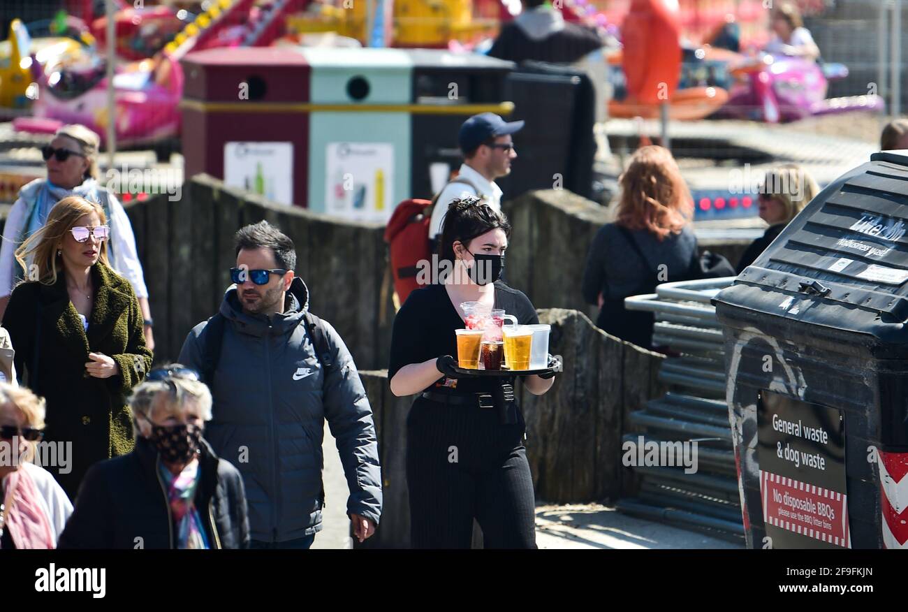 Brighton UK 18 aprile 2021 - il personale del bar fornisce le bevande mentre il lungomare e la spiaggia di Brighton sono occupati in una bella giornata di sole sulla costa meridionale: Credit Simon Dack / Alamy Live News Foto Stock