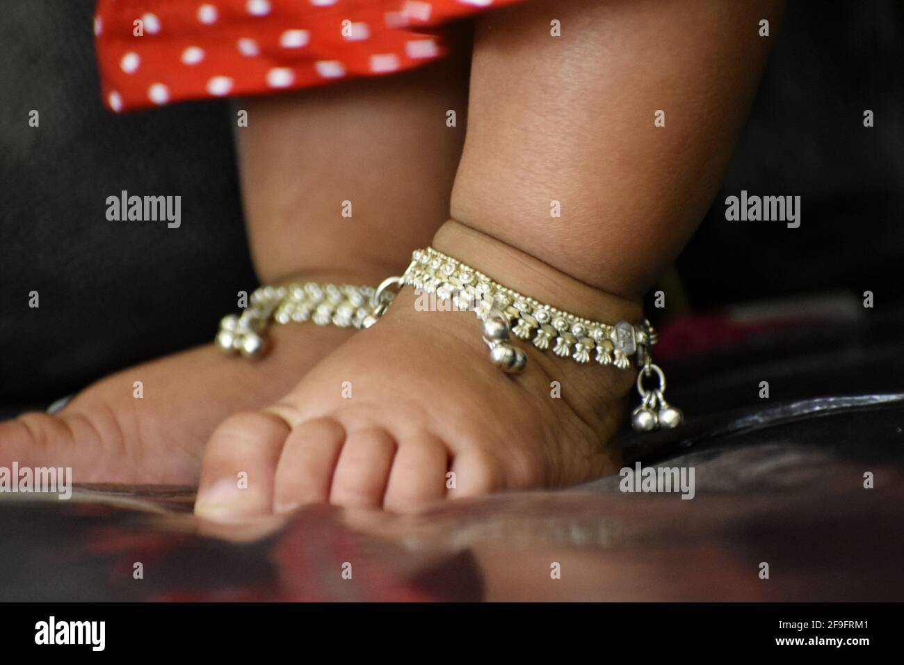 Una vista closeup di una caviglia argentata sui bambini piedi in piedi sul divano con un abito rosso Foto Stock