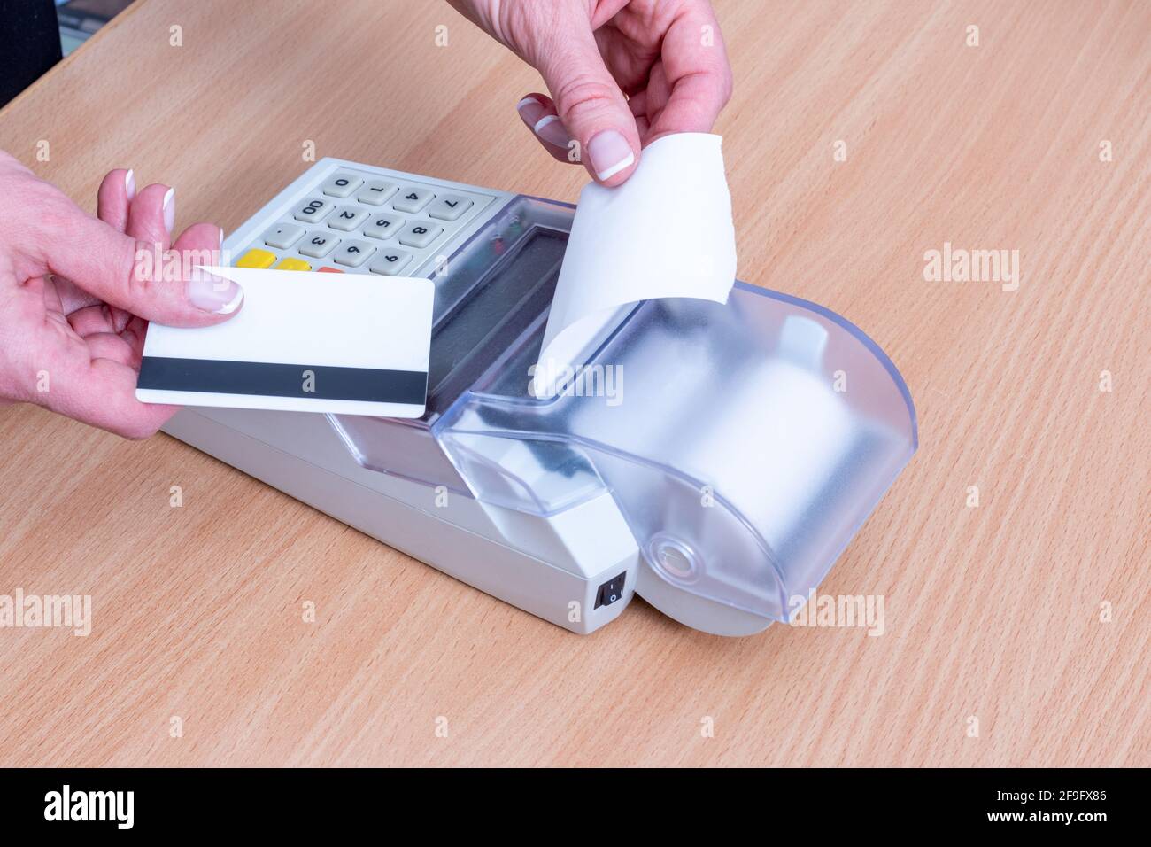 Concetto commerciale e finanziario. Primo piano di una mano che tiene una carta bancaria al di sopra del registratore di cassa per pagare un acquisto e una mano che strappare un assegno Foto Stock