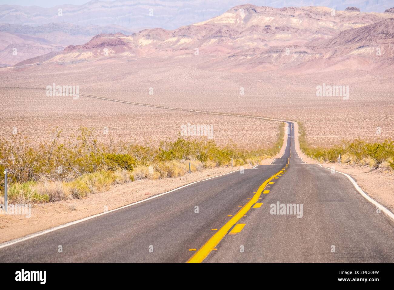 La linea gialla di traffico medio sulla Blacktop Empty Highway si estende in Far Horizon al Death Valley National Park Foto Stock