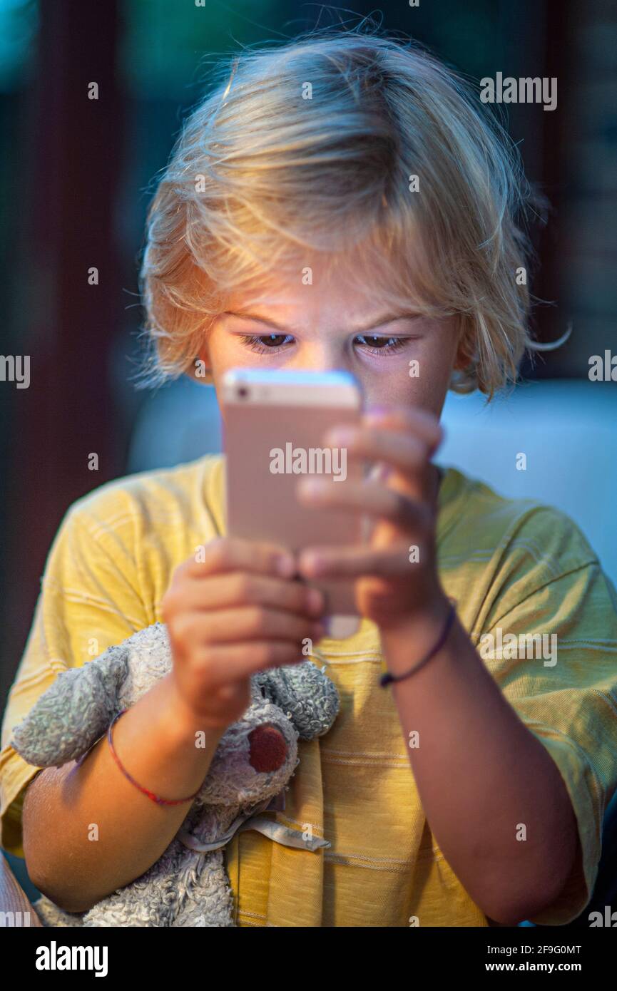 Bambino smartphone bambino di 4-6 anni ragazzo che stringe il vecchio giocattolo Dog concentrandosi sulle informazioni sullo schermo del suo smartphone iPhone Foto Stock