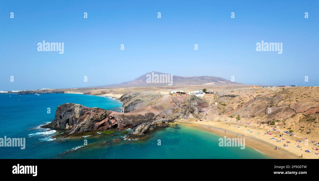 Playa Blanca, Lanzarote, Isole Canarie, Spagna. Vista panoramica lungo la costa dalla cima della scogliera sopra Playa del Papagayo, Atalaya de Femés sullo sfondo. Foto Stock